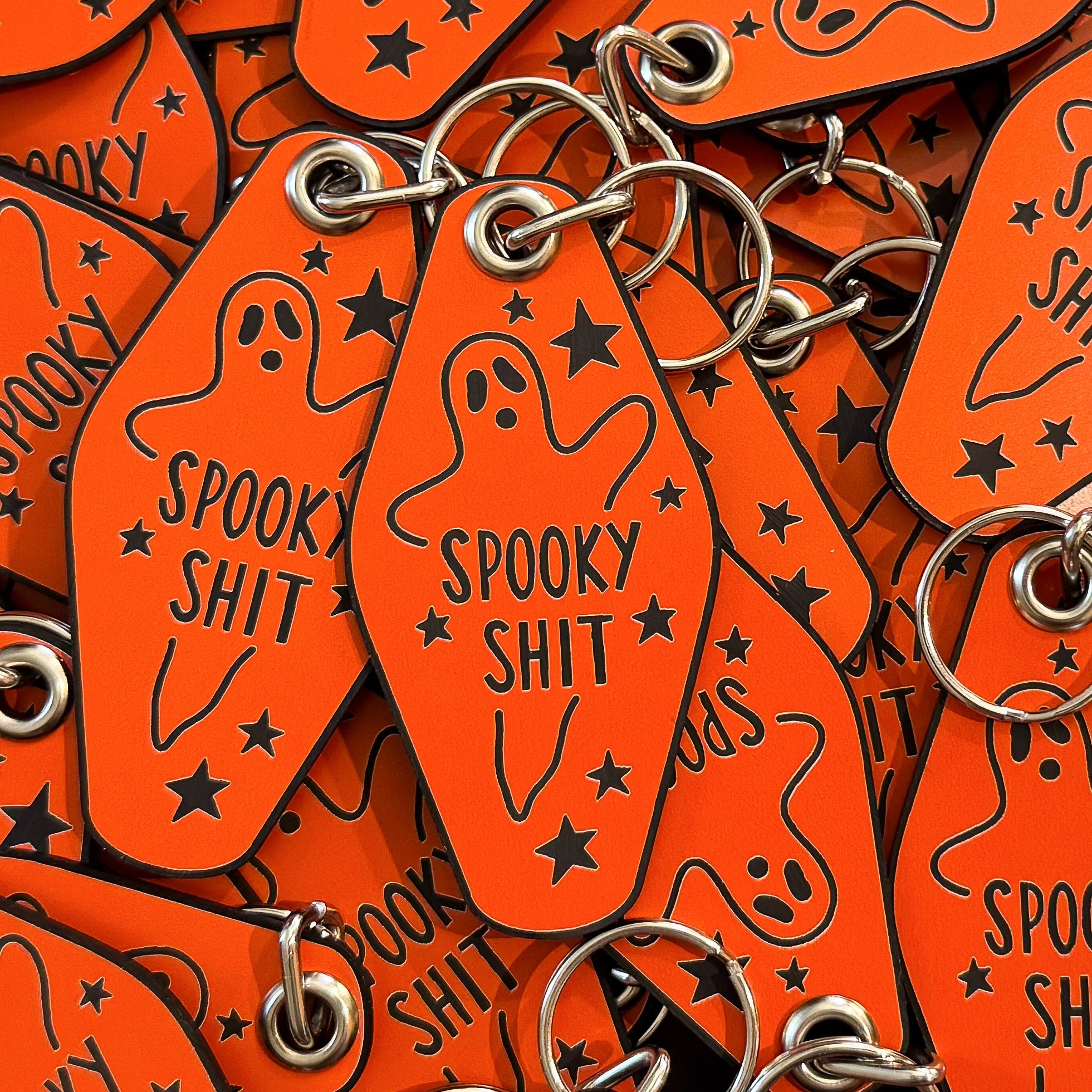 A pile of orange keychains that say 'SPOOKY SHIT' in the middle of a drawing of a ghost.