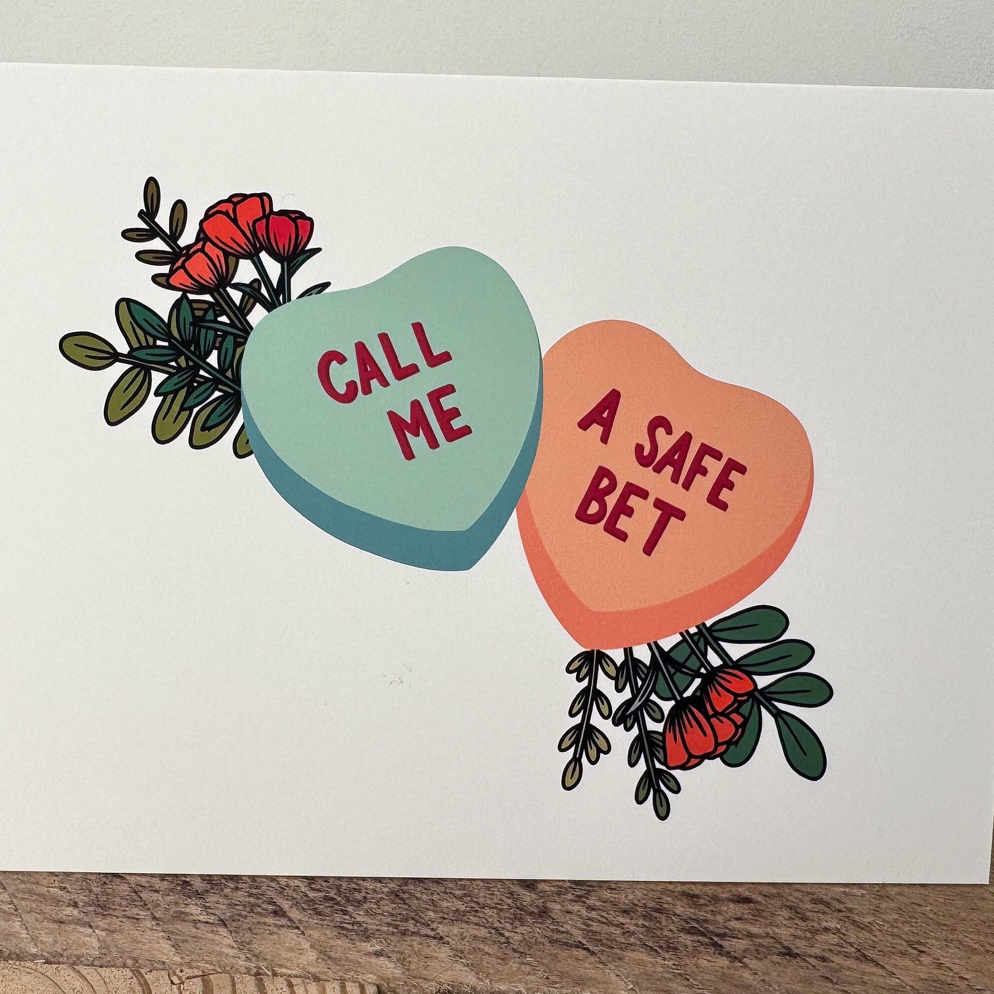 A greeting card with two conversation hearts that say "call me" and "a safe bet" in red with flowers coming out from behind them.