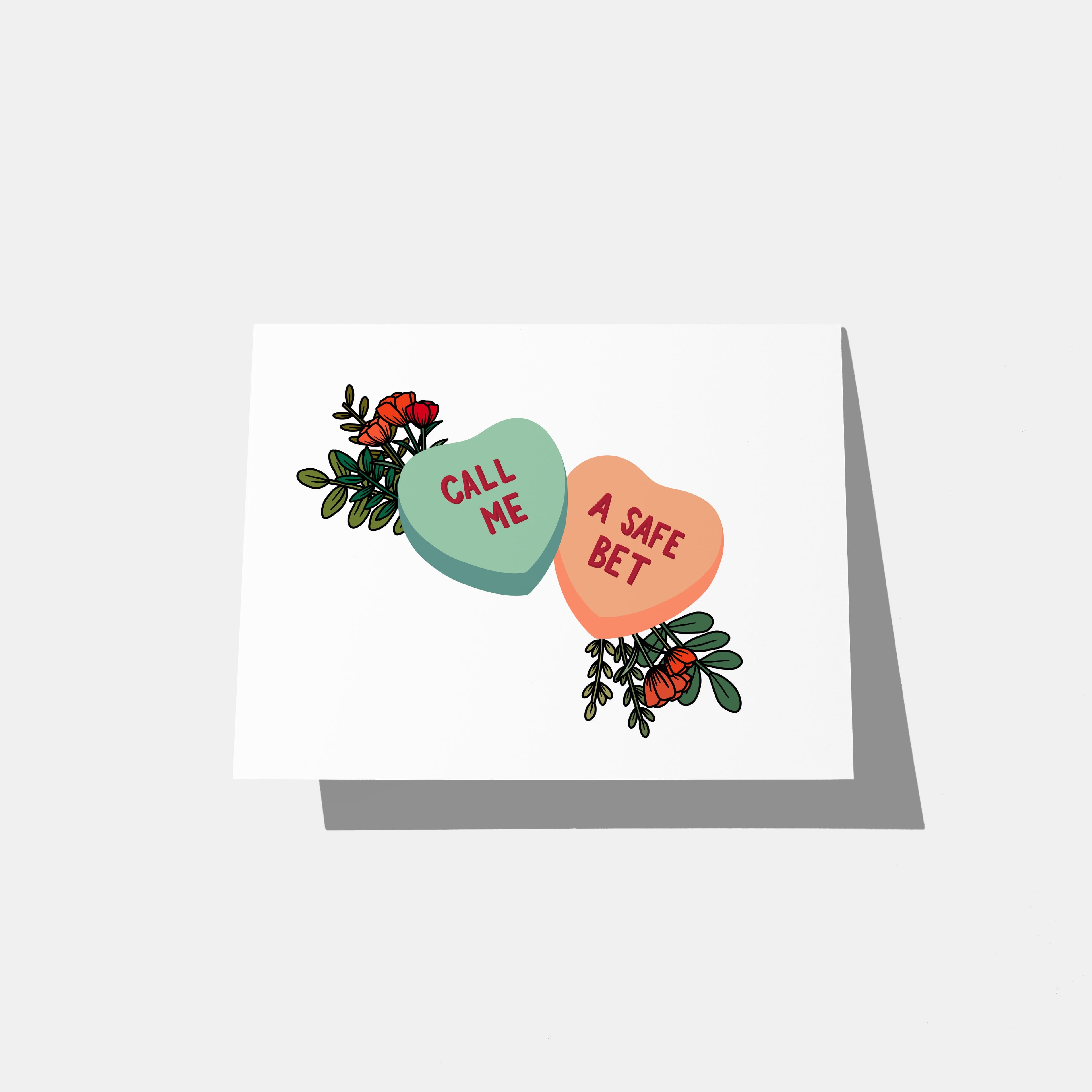 A mockup of a greeting card with two conversation hearts that say "call me" and "a safe bet" in red with flowers coming out from behind them.
