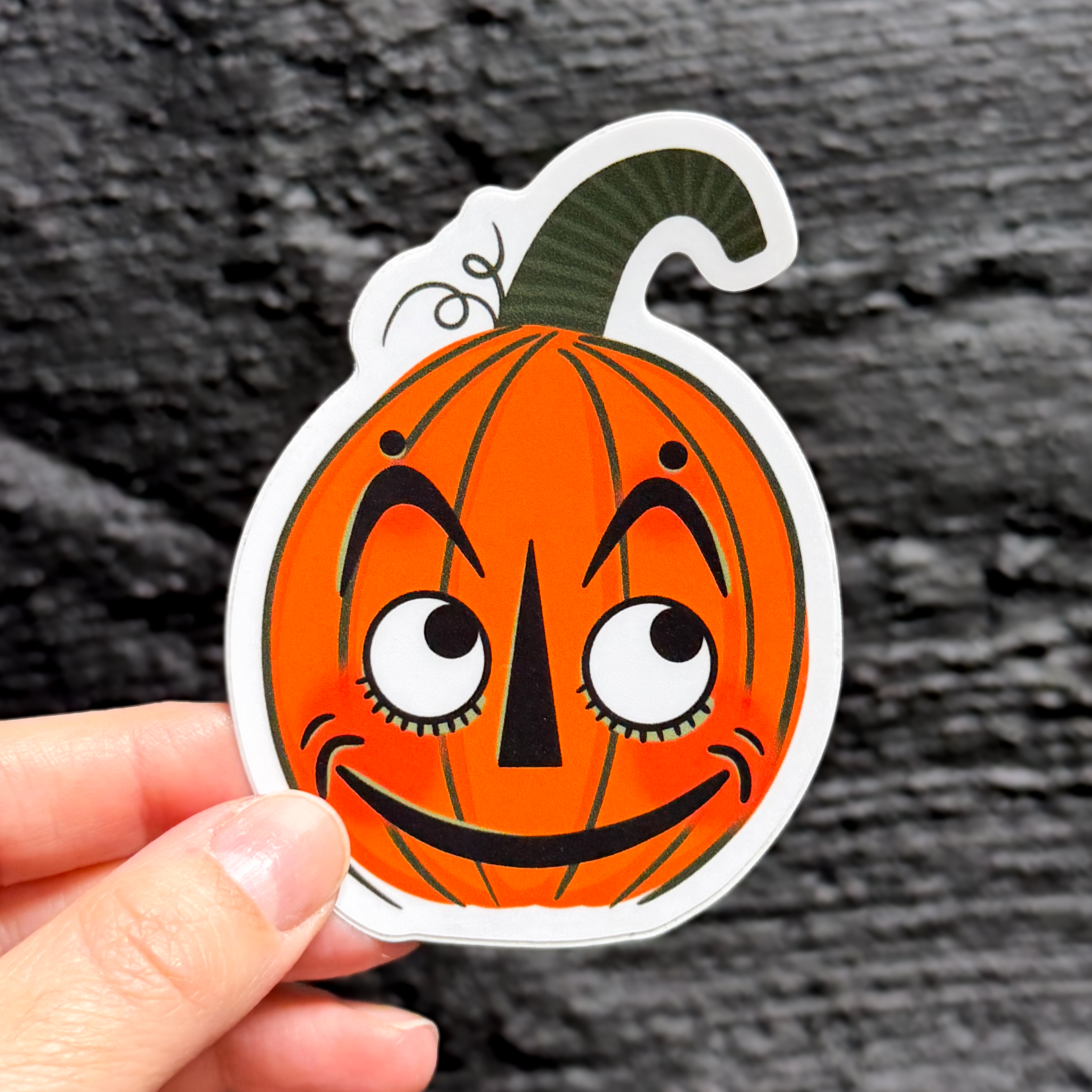 A hand holding a vintage halloween pumpkin sticker with a cute face.