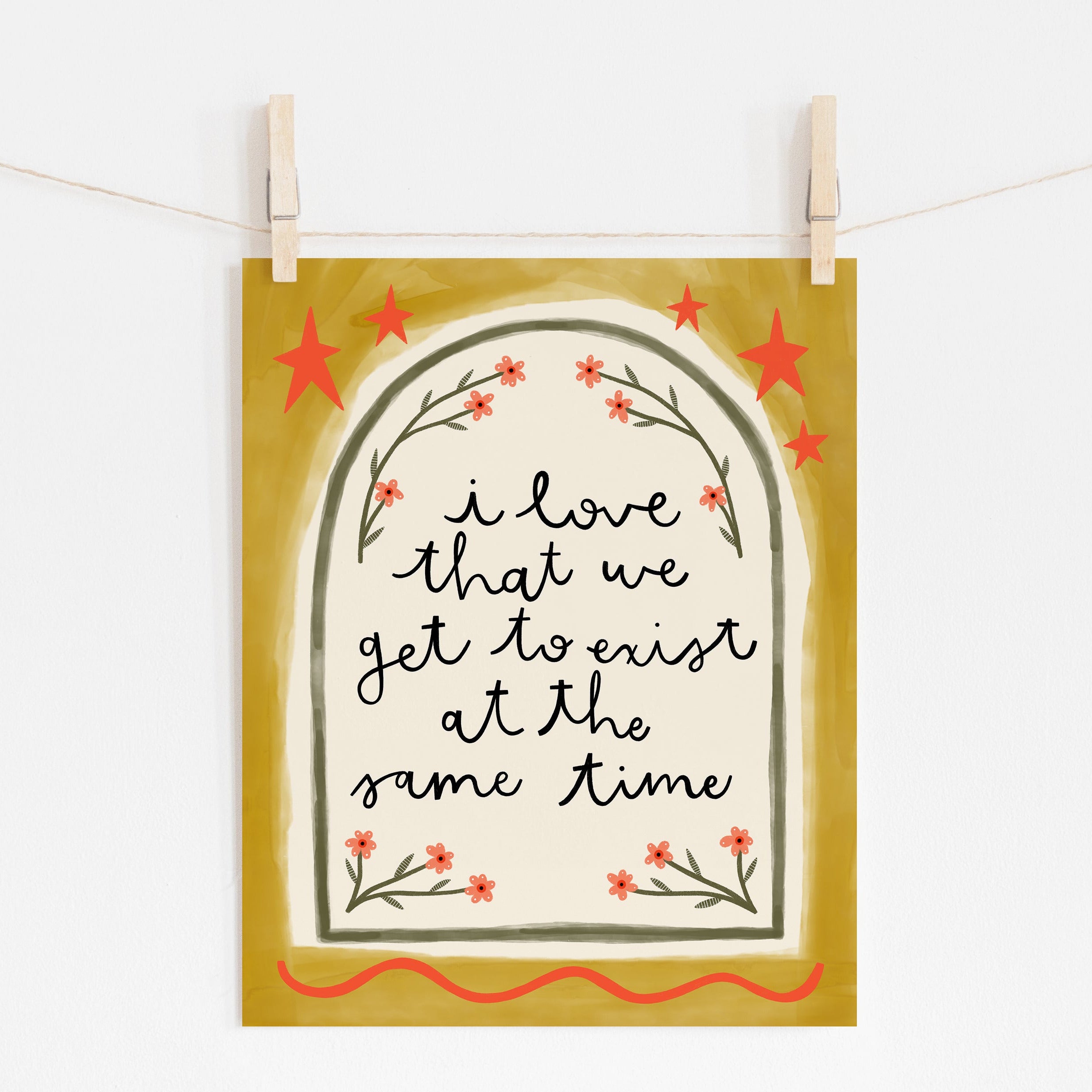 An 8x10 yellow print that says 'i love that we get to exist at the same time' inside a cream and green arch with little flowers framing it and red stars and embellishments on the edge.