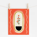 An 8x10 art print with a red/orange background, cream oval and squiggles on the sides. Inside the oval is a yellow outline and four pink flowers sitting above a black half circle. 