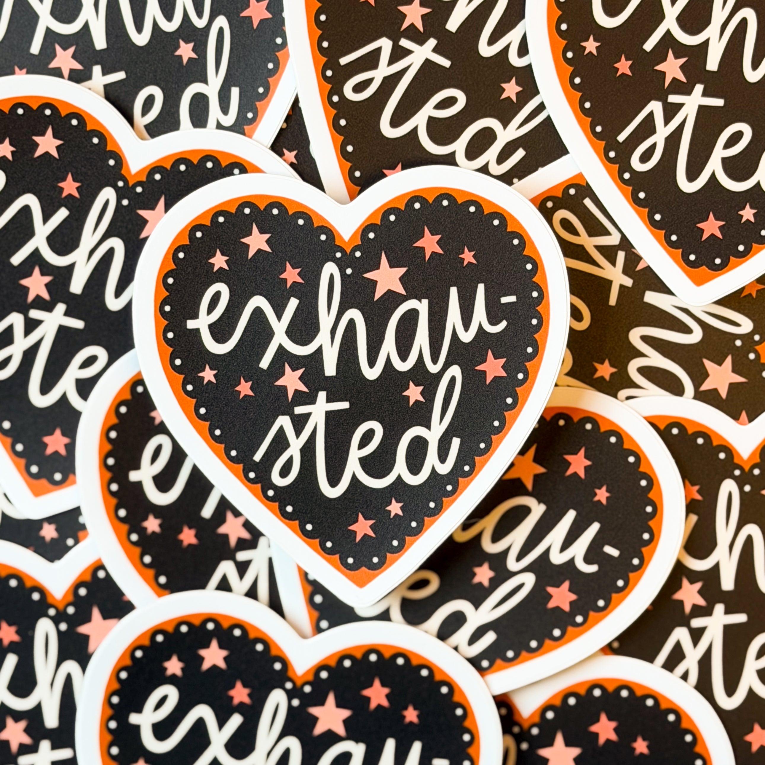 A pile of heart-shaped stickers with 'exhausted' text and star patterns on a black and orange background.