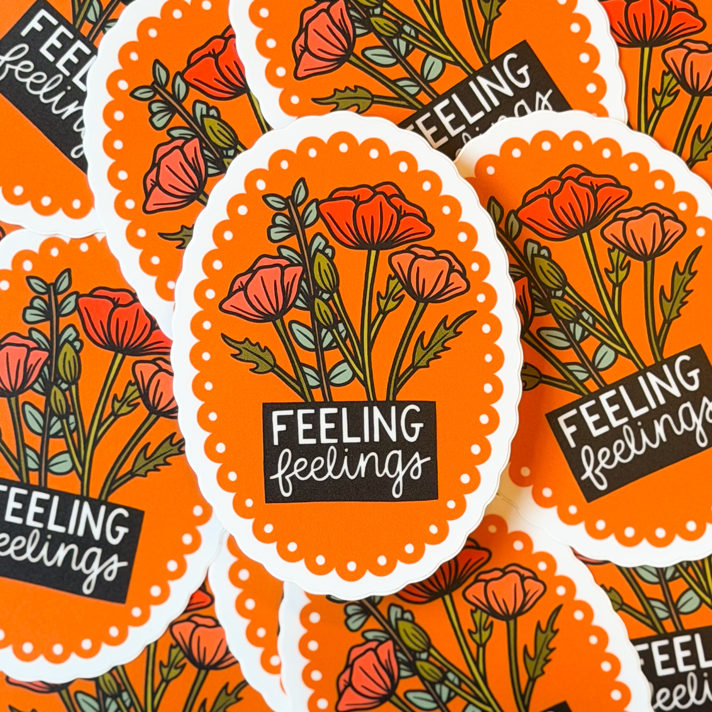 A pile of stickers with scalloped floral design and 'FEELING feelings' text on an orange background.