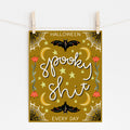 A mockup of an 8x10 Halloween art print with a yellow background that says "spooky shit" in the middle and "HALLOWEEN EVERY DAY" framing the top and bottom. There are spiderwebs, bats, crescent moons, stars, and flowers embellishing it. 