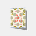 A mockup of a greeting card against a dark textured background. The card has a white base with sage green polka dots, yellow floral sprigs, pink squiggly lines, and red text that reads, 'I AM SO LUCKY TO KNOW YOU'.