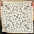 Natural color bandana with black floral patterns and 'I CRY A LOT' text held up by two hands.