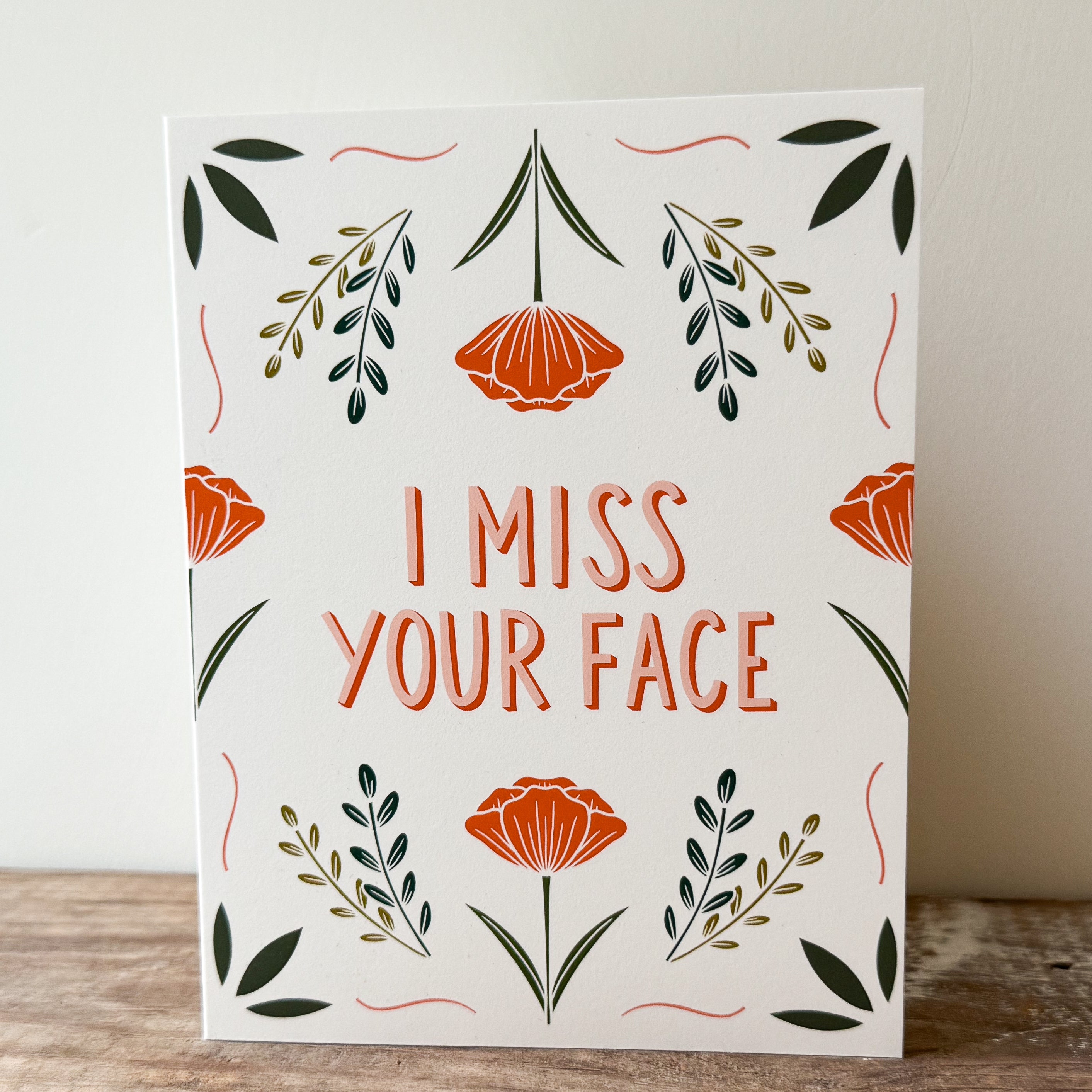 A greeting card with floral design and text 'I MISS YOUR FACE' on a white background.