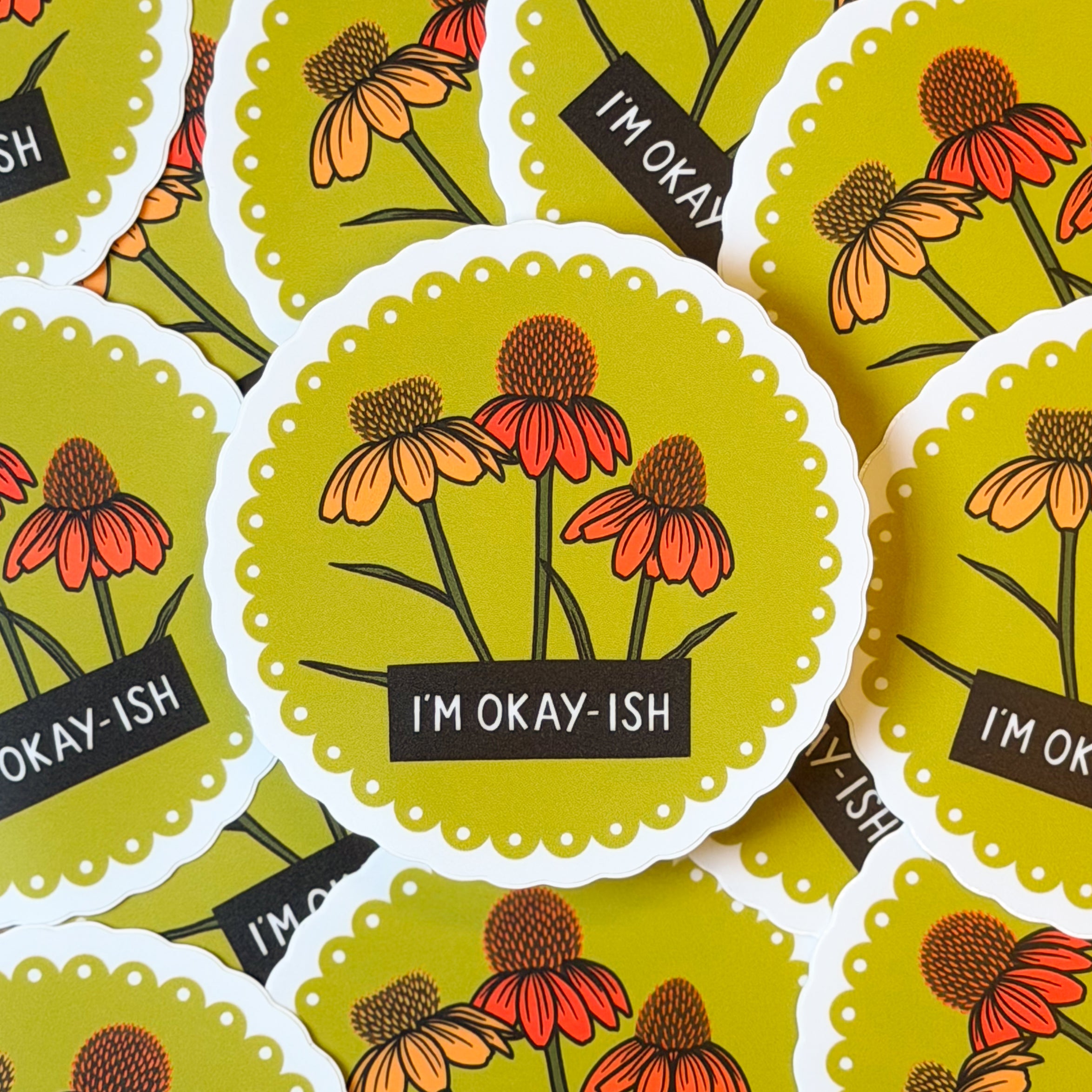 A pile of stickers with a floral design and 'I'm okay-ish' text on a yellow scalloped background.