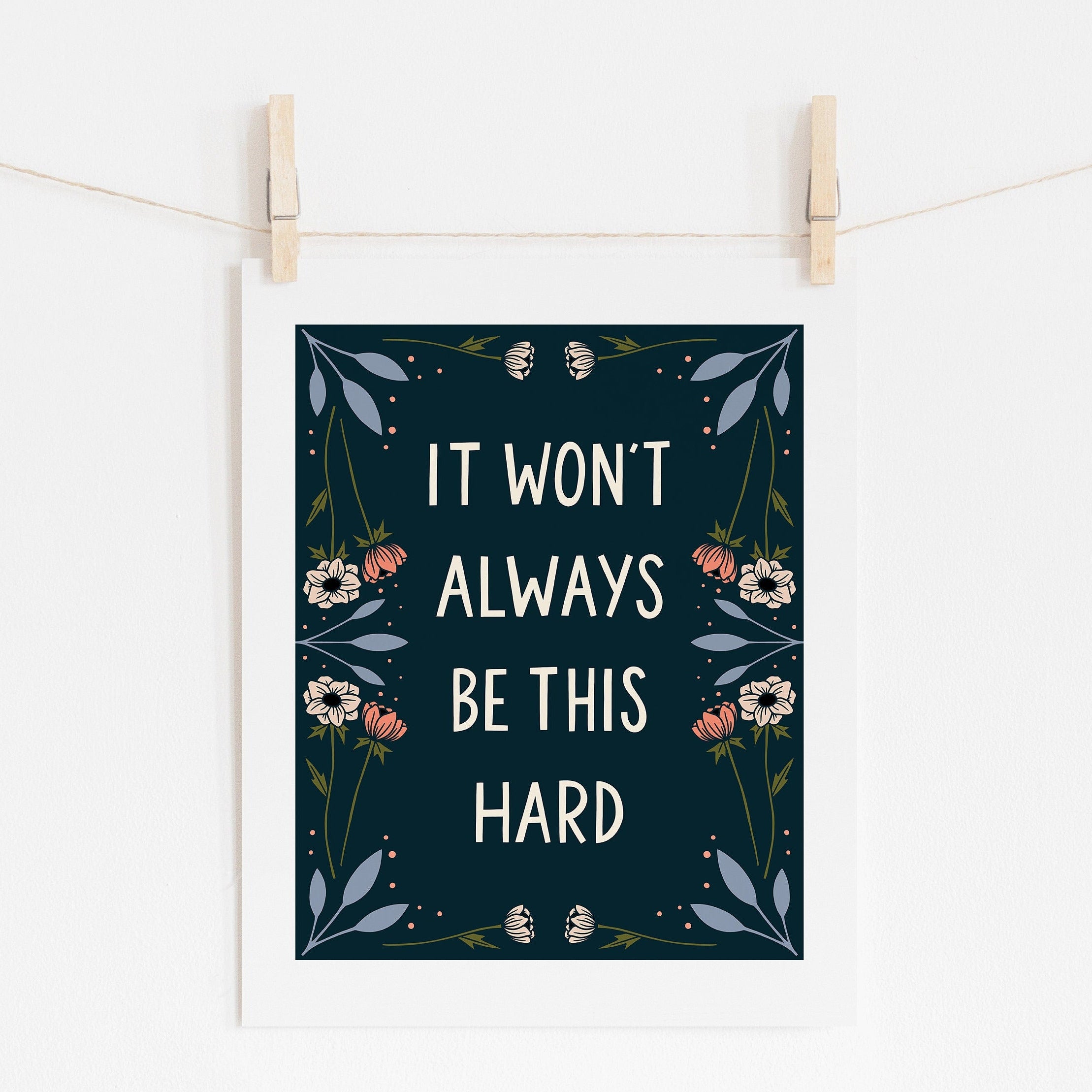 An 8x10 art print with dark blue background that says 'IT WON'T ALWAYS BE THIS HARD' in cream surrounded by cream,  pink, and blue flowers.