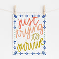 An 8x10 art print that says 'just trying to survive' in cursive lettering in slight gradient colors from red to yellow. A border of blue and light blue embellishments surrounds it.