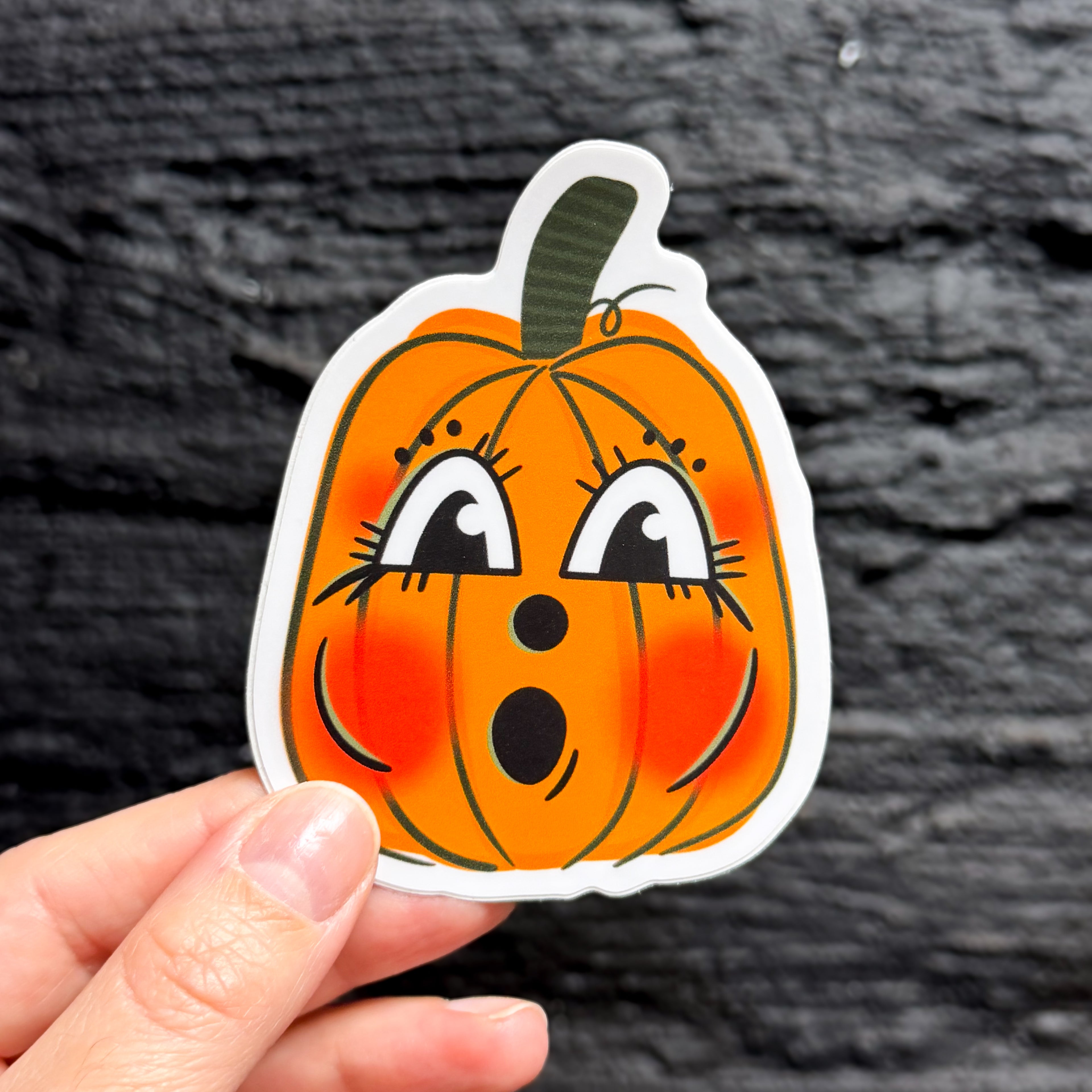 A hand holding a vintage halloween pumpkin sticker with a cute face.