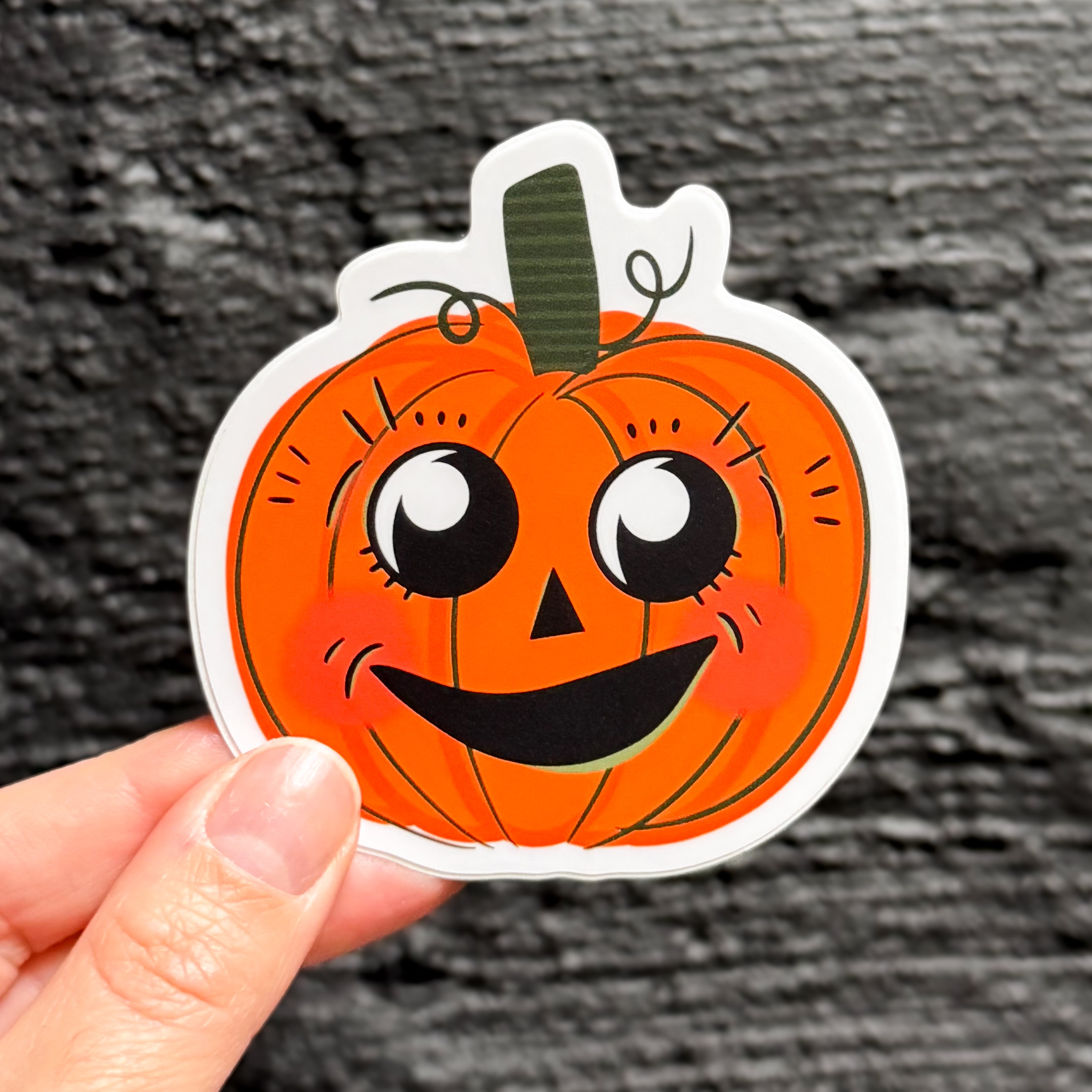 A hand holding a vintage halloween pumpkin sticker with a cute face.