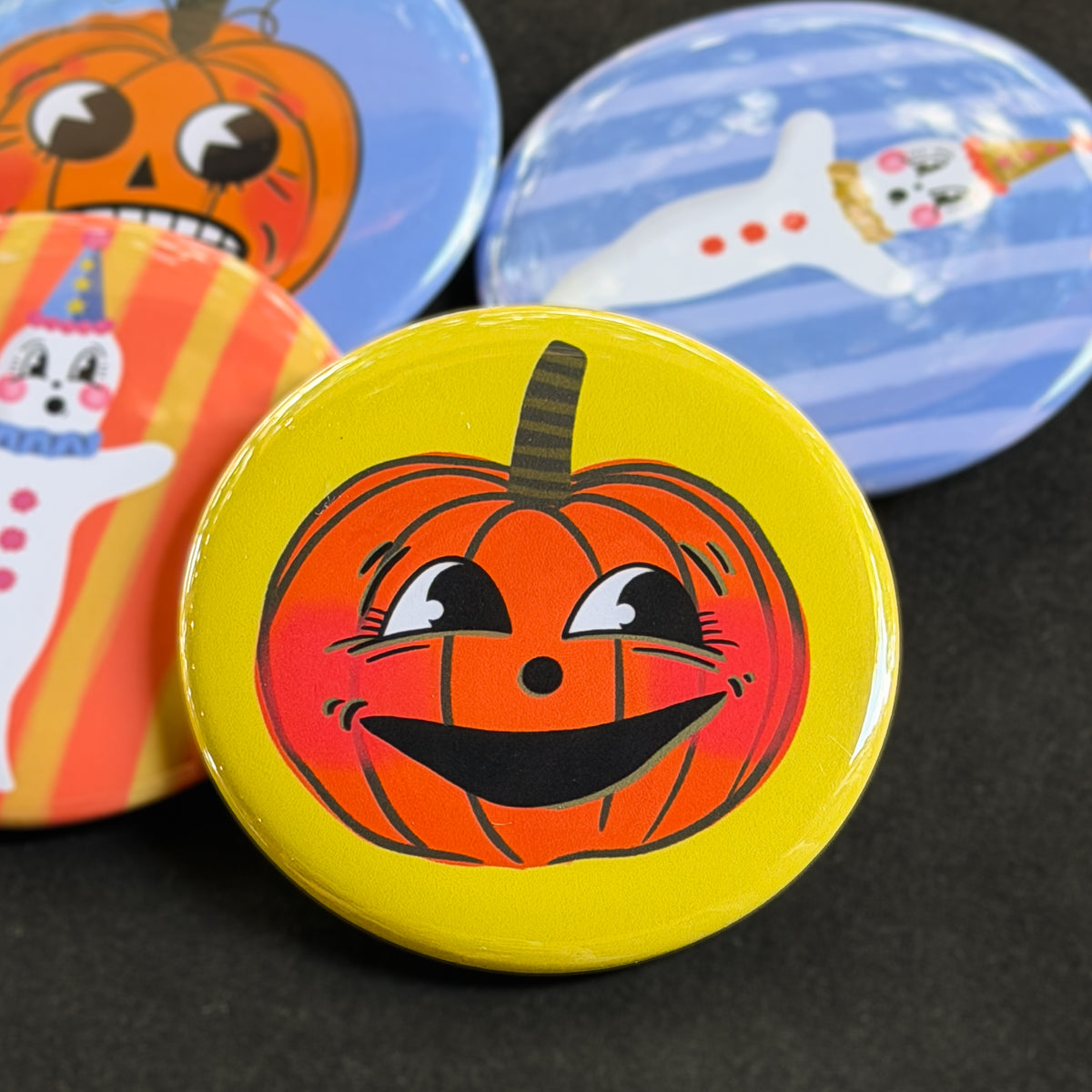 A round pinback button featuring a happy orange pumpkin named Clementine with a yellow background. The pin is surrounded by other pin designs.