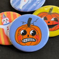 A round pinback button featuring a nervous orange pumpkin named Theo with a blue background. The pin is surrounded by other pin designs.
