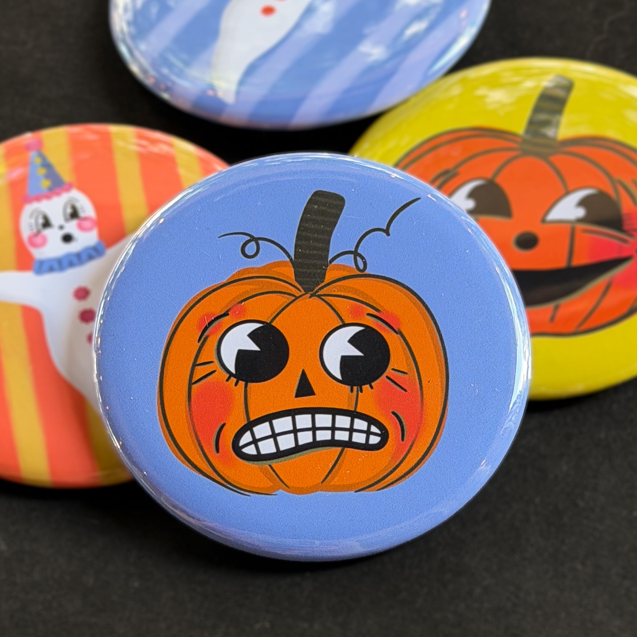 A round pinback button featuring a nervous orange pumpkin named Theo with a blue background. The pin is surrounded by other pin designs.