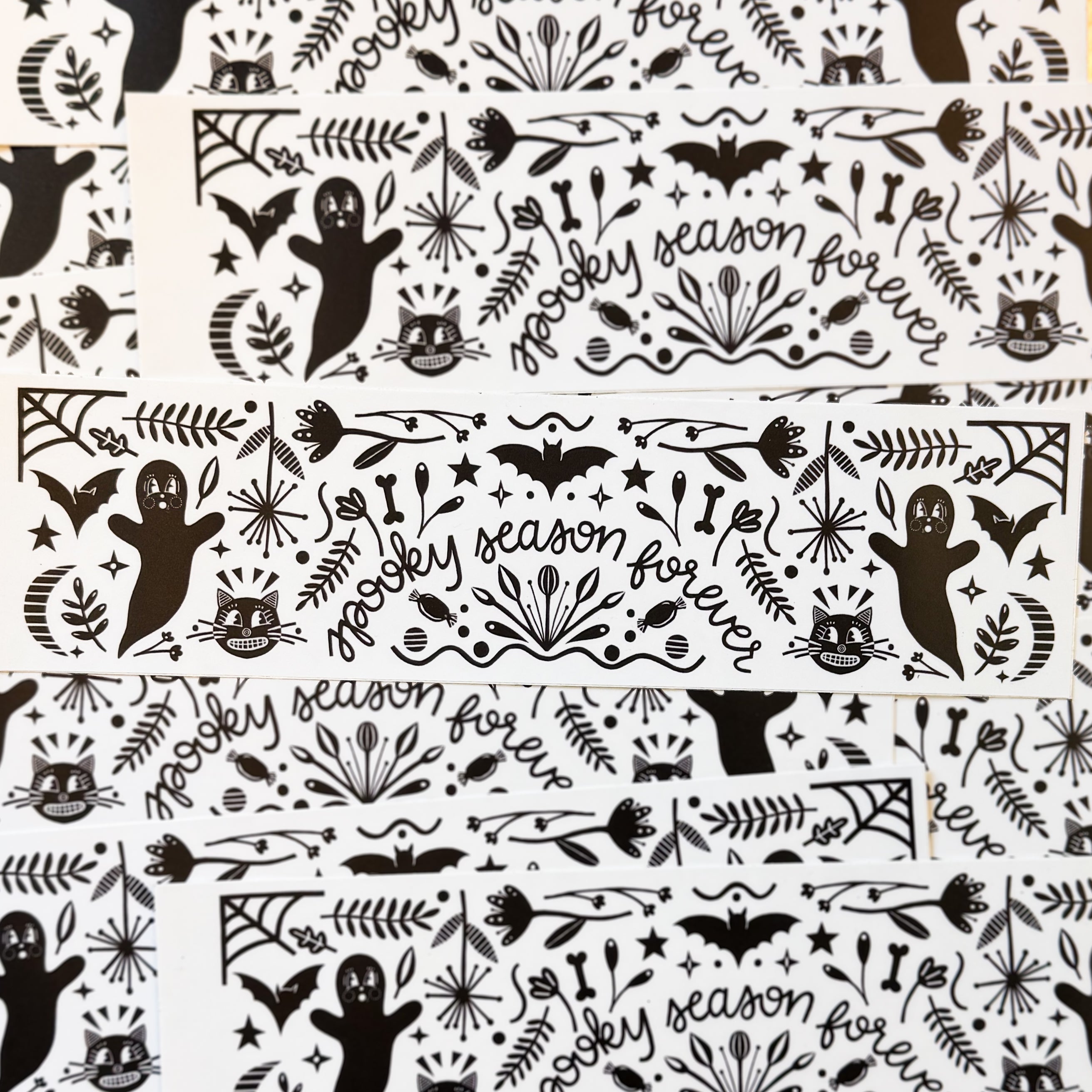 A pile of black and white bumper stickers that say 'spooky season forever' surrounded by ghosts, bats, cats, and other halloween whimsy.