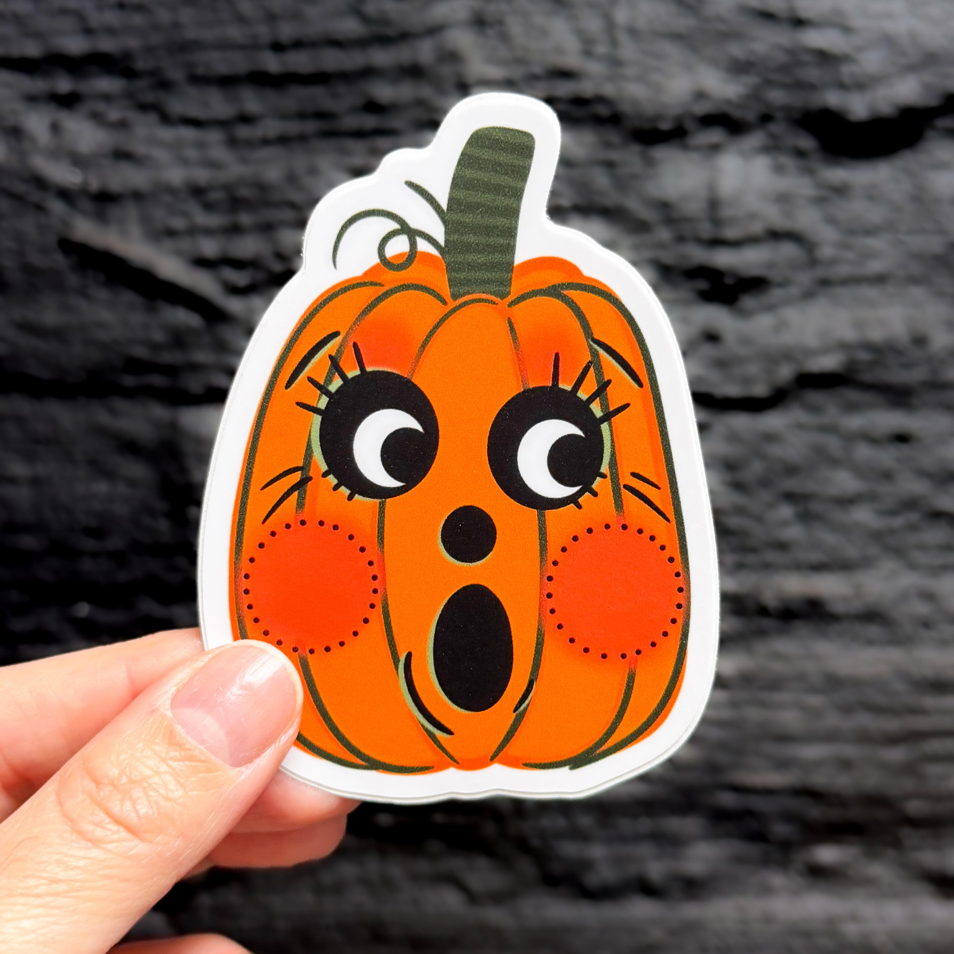 A hand holding a vintage halloween pumpkin sticker with a cute face.