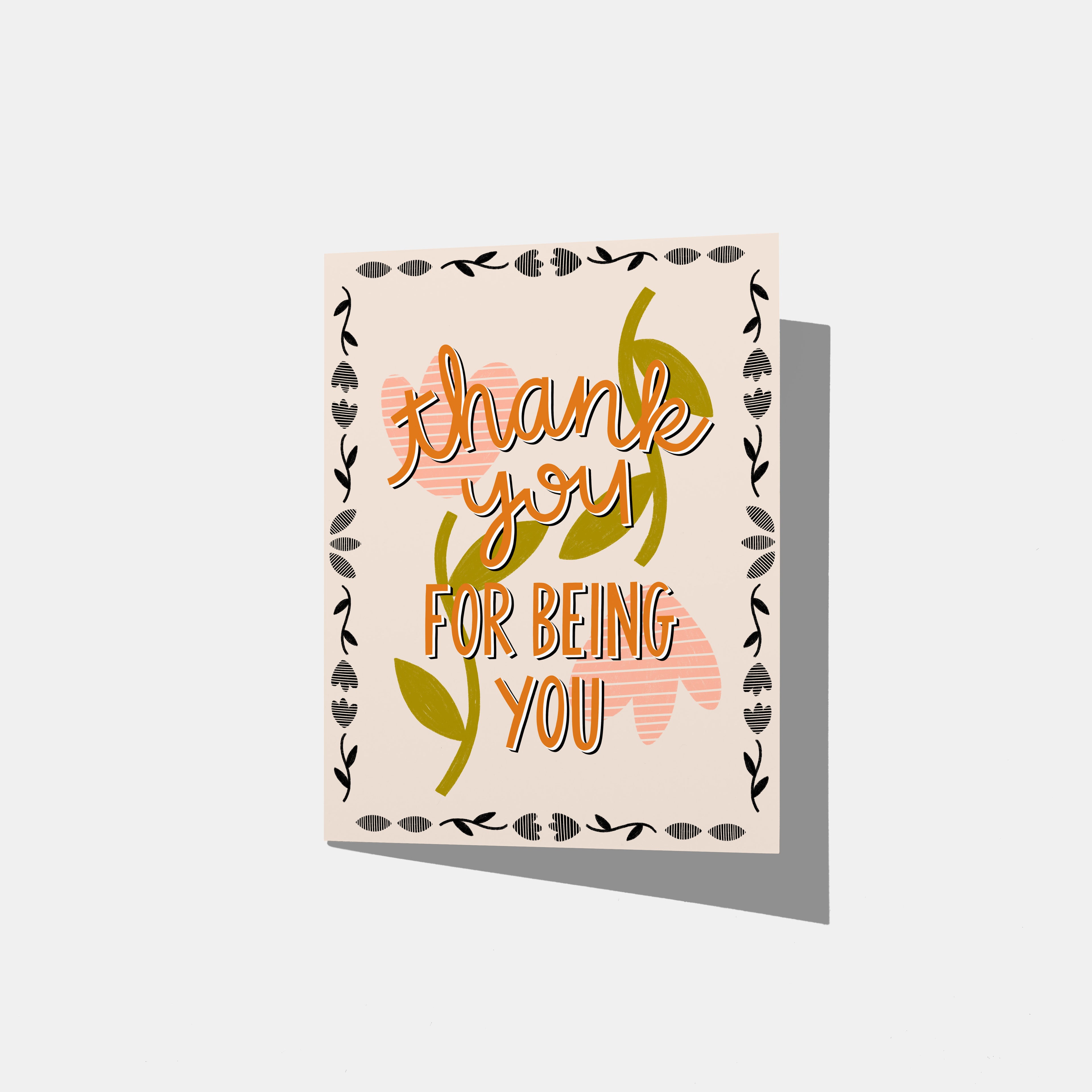 A mockup of a greeting card with 'thank you FOR BEING YOU' in orange text with a peach flower background and border of little black flowers.