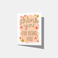 A mockup of a greeting card with 'thank you for being you' text in green with a red drop shadow and star decorations on a  peach cloud-like shape on a white background.