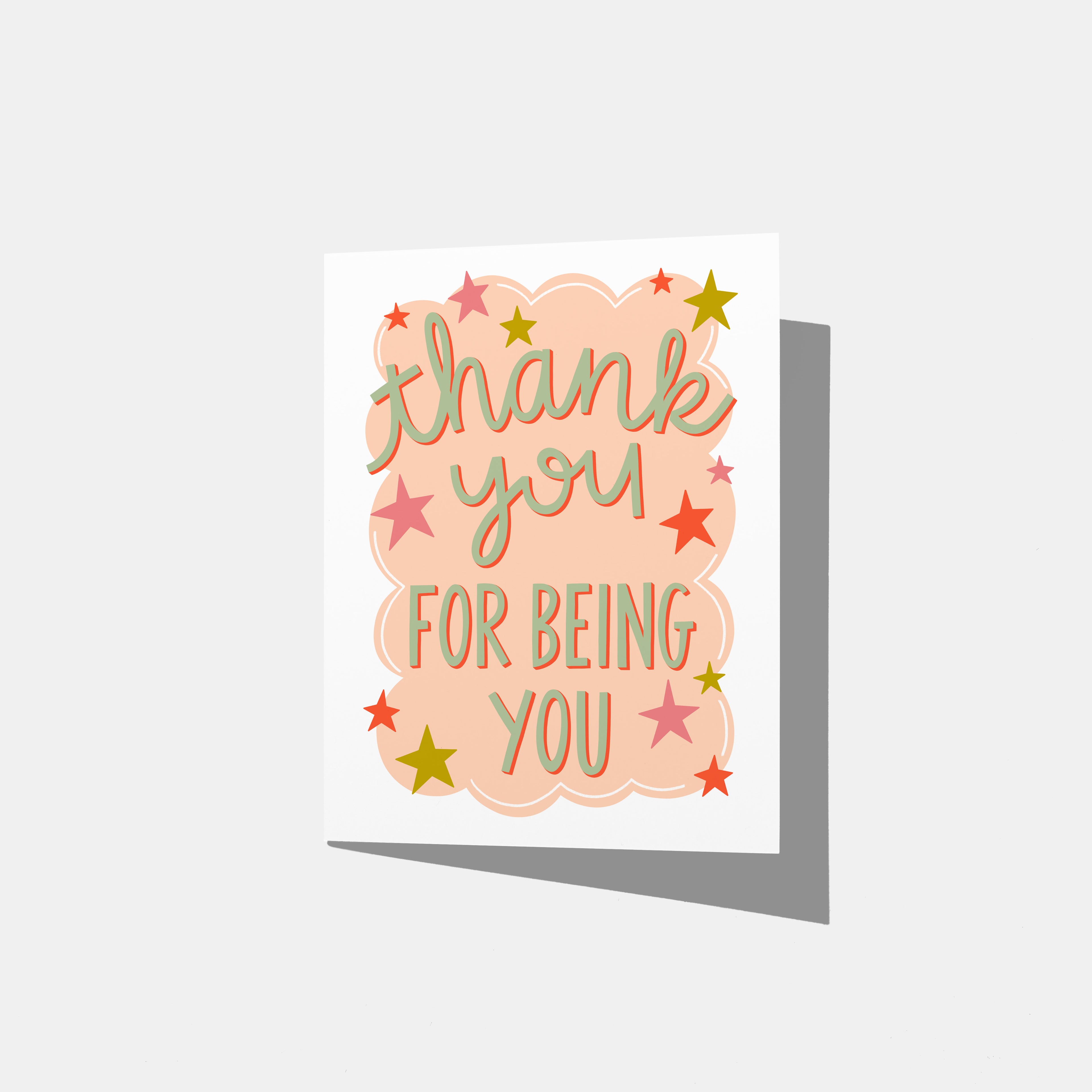 A mockup of a greeting card with 'thank you for being you' text in green with a red drop shadow and star decorations on a  peach cloud-like shape on a white background.