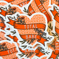 A pile of heart stickers with 'TOTAL BABE' written on a floral banner.