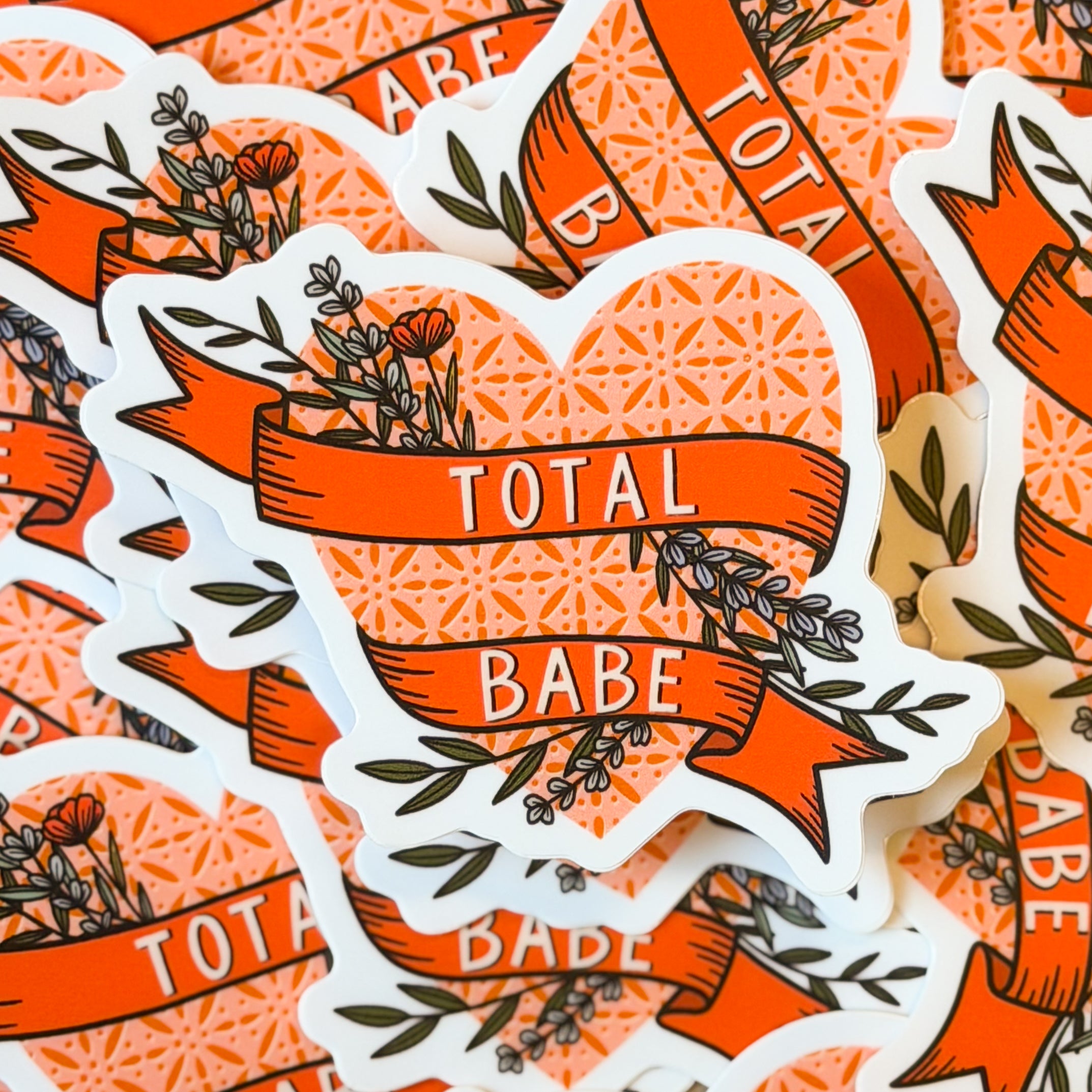 A pile of heart stickers with 'TOTAL BABE' written on a floral banner.