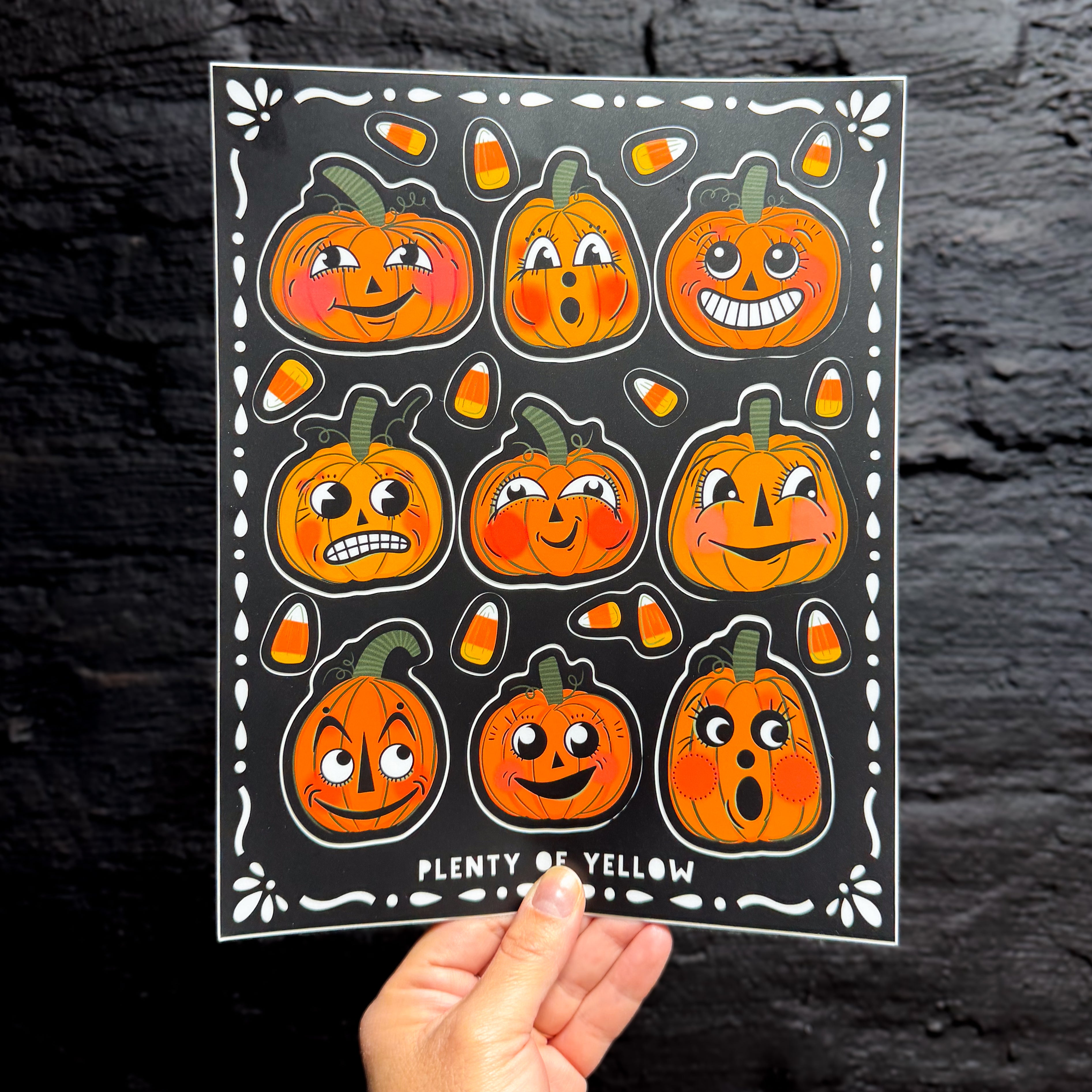 A hand holding a sticker sheet with vintage pumpkins and candy corn on it.