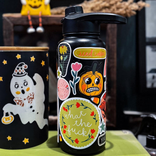 Stickers on a black water bottle next to a ghost canister with decor in the background.