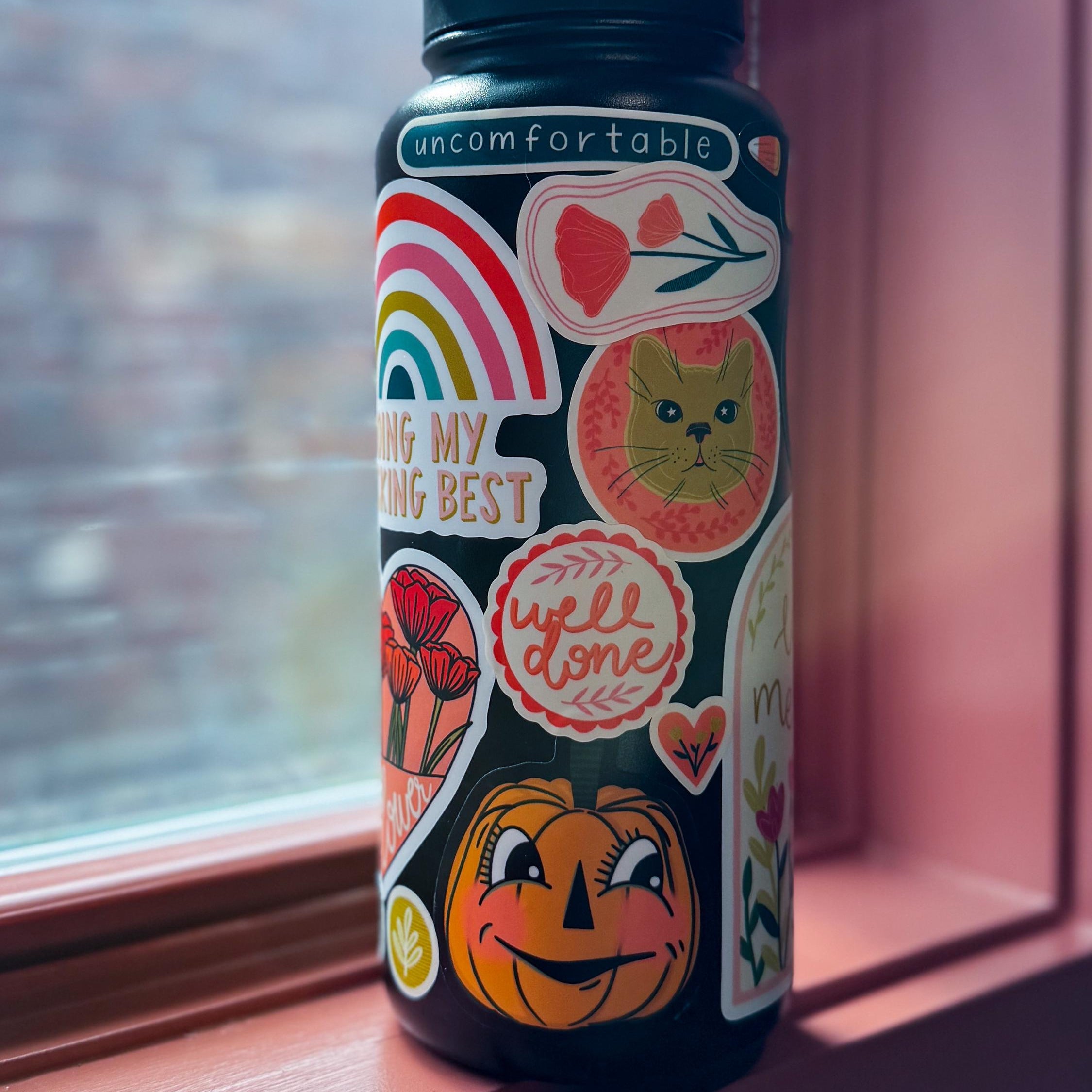 Stickers on a black water bottle sitting on a window sill.