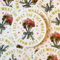 A pile of stickers with floral design and text 'WHAT THE FUCK' on a white background