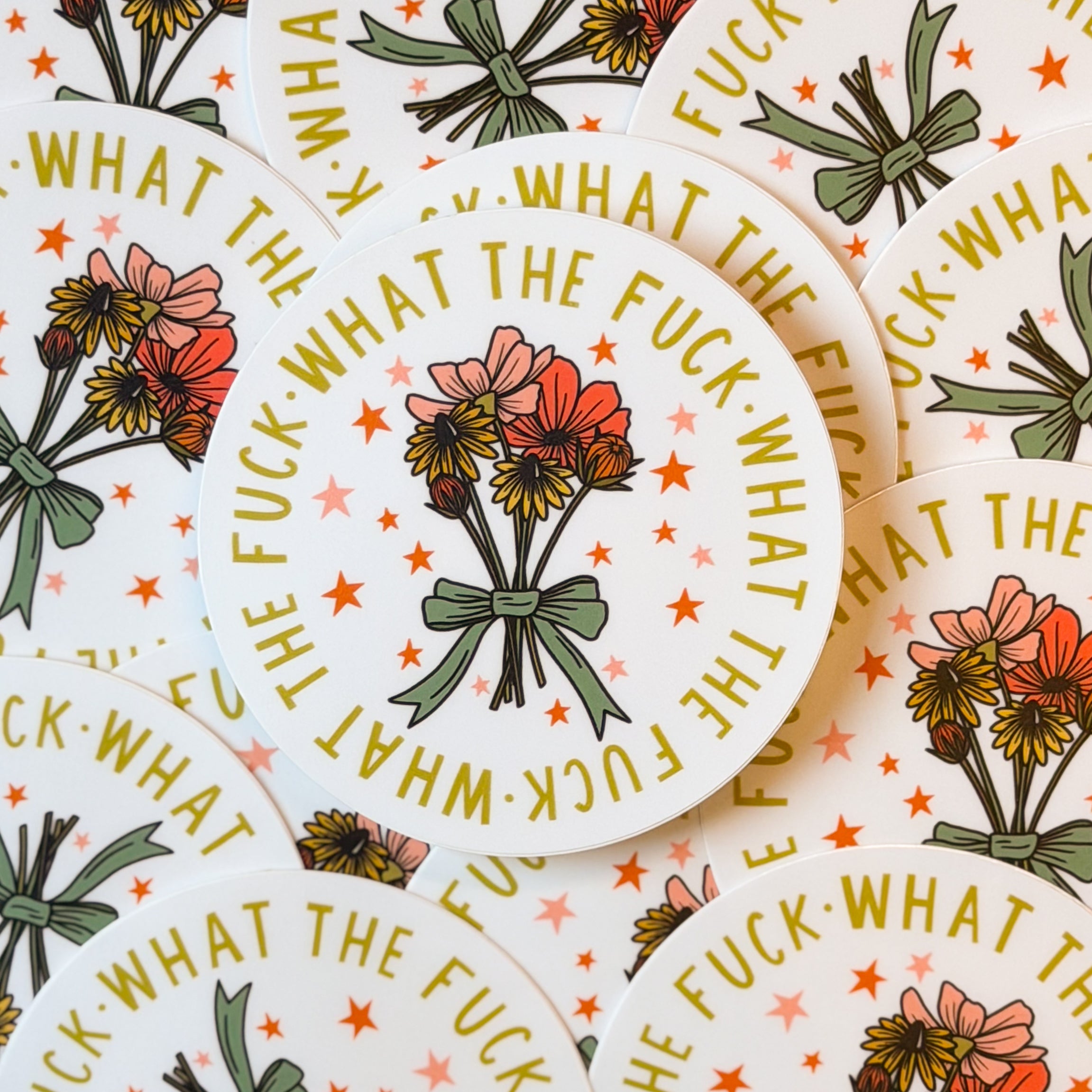 A pile of stickers with floral design and text 'WHAT THE FUCK' on a white background