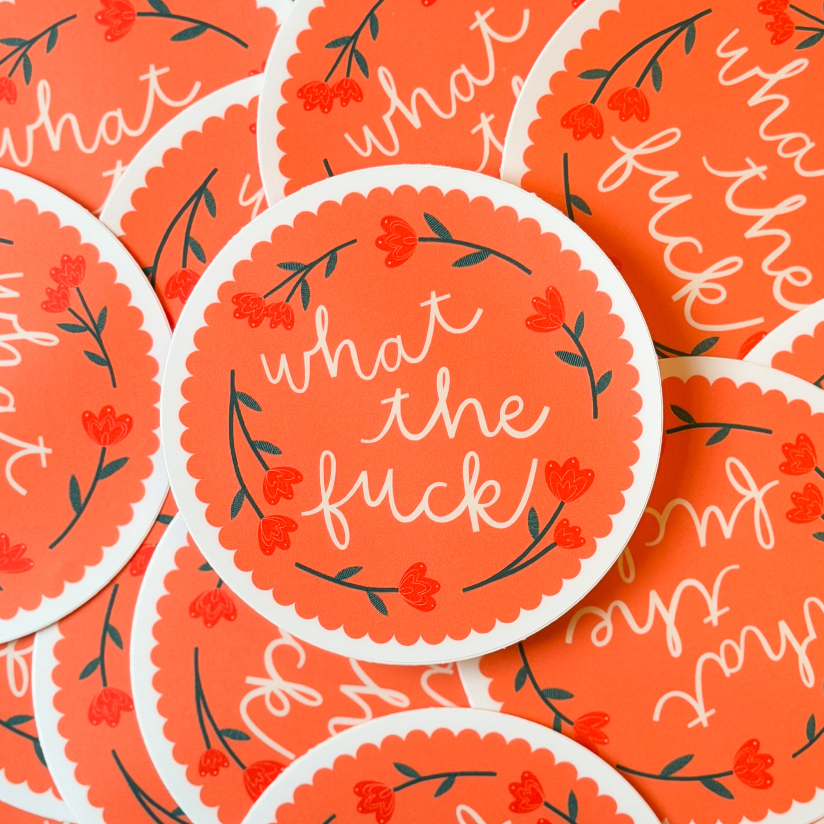A pile of circular stickers with floral designs and text 'what the fuck' on a peach scalloped background.