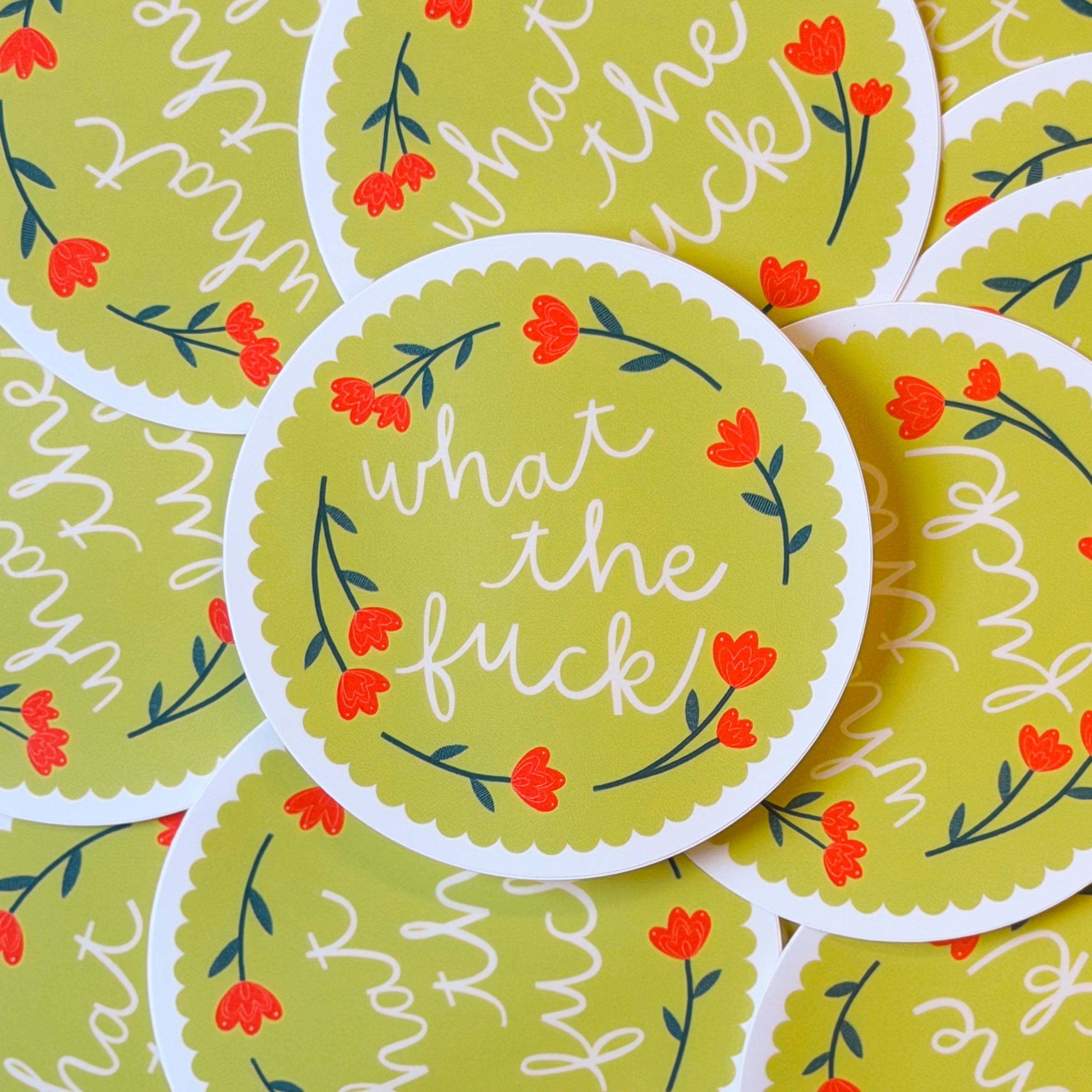 A pile of circular stickers with floral designs and text 'what the fuck' on a yellow scalloped background.