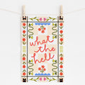 An 11x17 art print with a peach checkered background that says 'what the hell' in the middle, surrounded by folk art style flowers and cats with party hats in the corners.