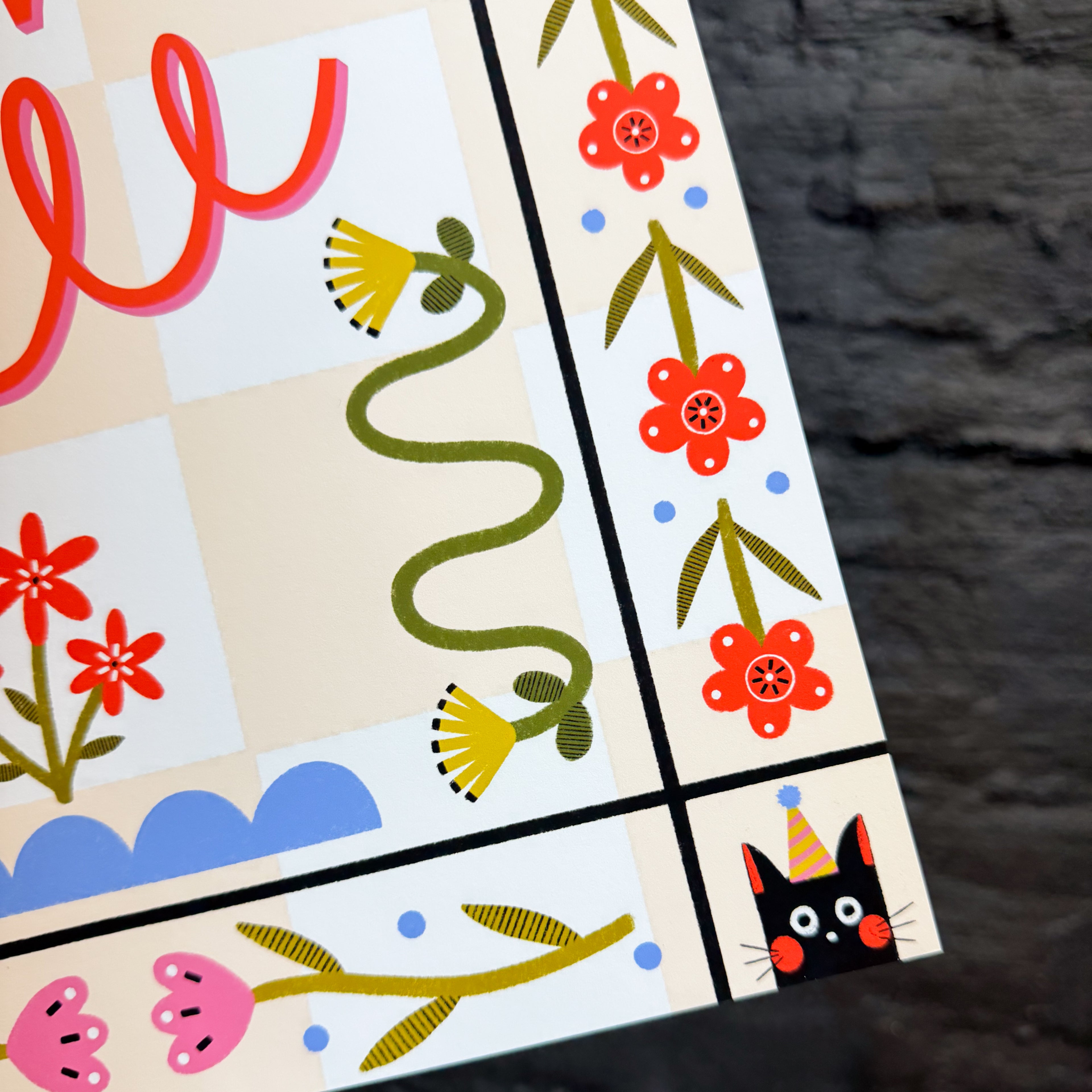 An up close of an 11x17 art print with a peach checkered background that says 'what the hell' in the middle, surrounded by folk art style flowers and cats with party hats in the corners.