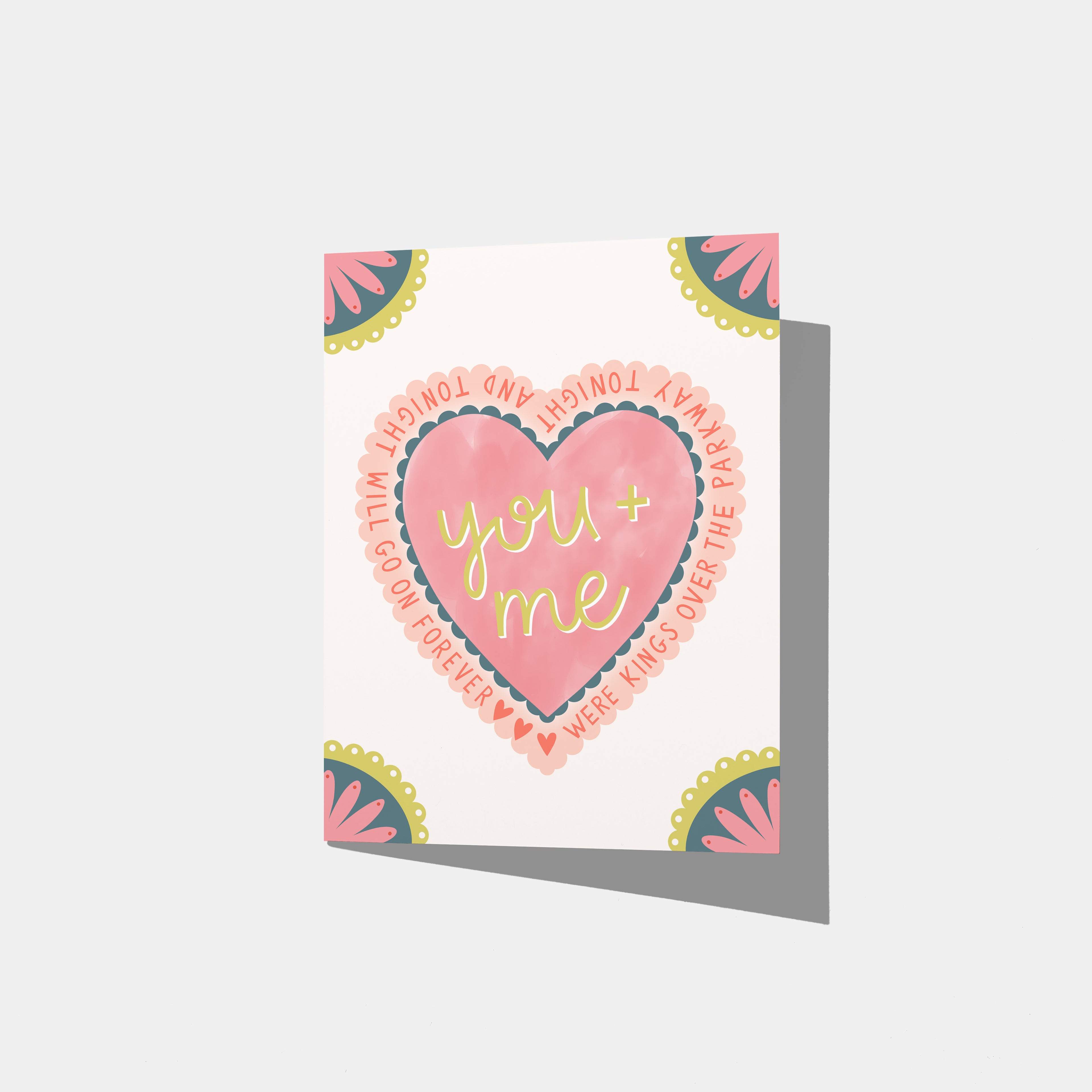 A mockup of a greeting card with a heart in the middle that says 'you and me were kings over the parkway tonight and tonight will go on forever' with three small hearts to fill space. All four corners are embellished with a scalloped flower.